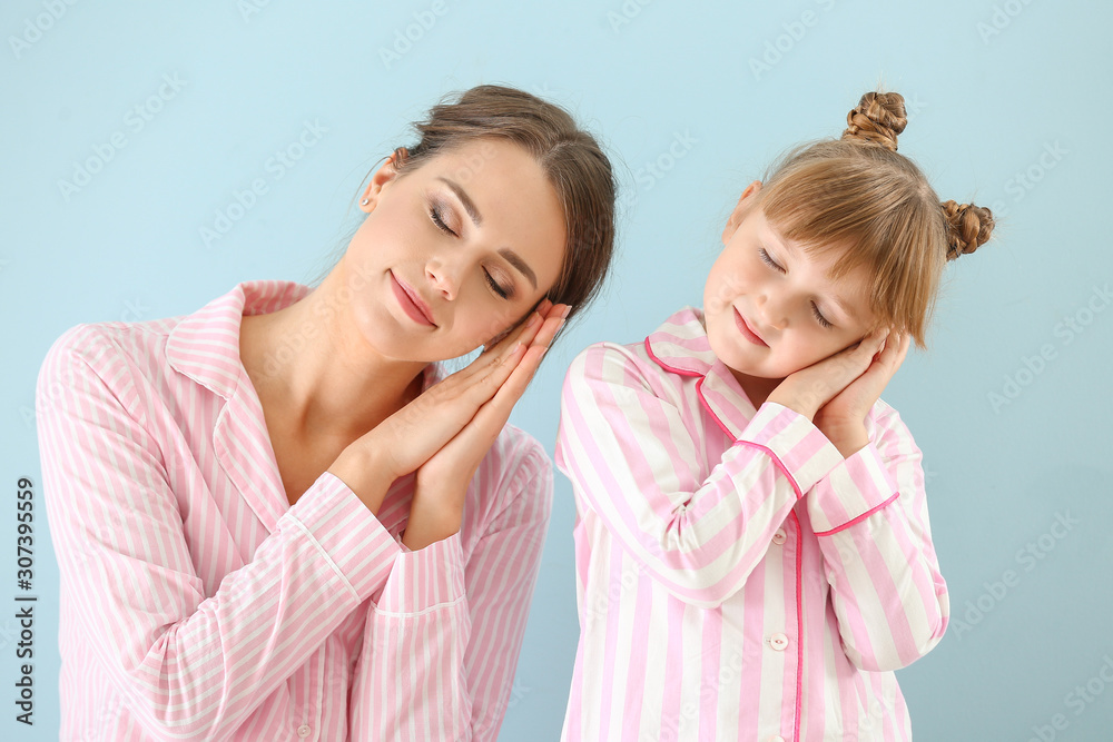 Portrait of sleepy mother and daughter in pajamas on color background