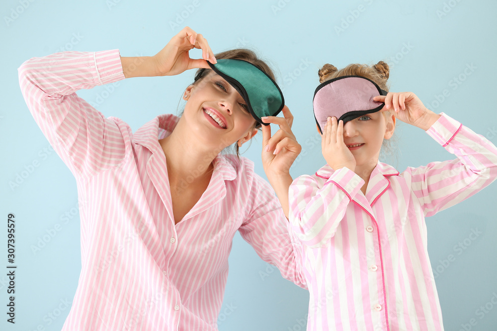 Portrait of happy mother and daughter in pajamas and with sleep masks on color background