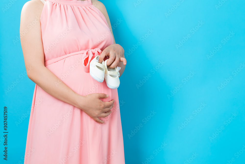 Pregnant woman on a solid background holding baby shoes