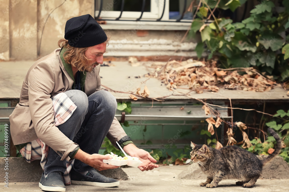 Poor man sharing food with homeless cat outdoors