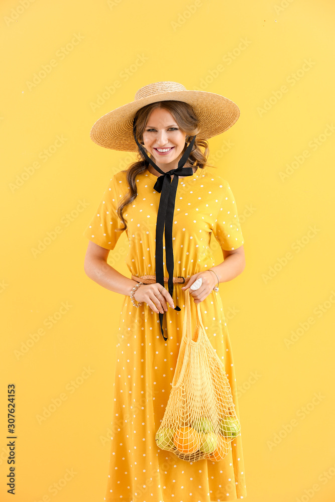 Fashionable young woman holding mesh bag with fruits on color background