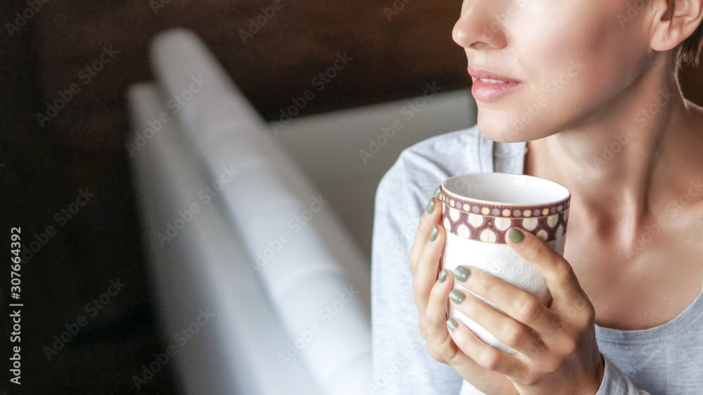 年轻女子在白色厨房里用晨光喝咖啡或茶