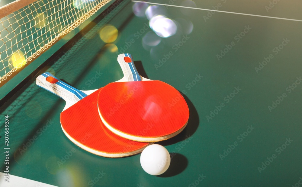 Two ping pong rackets and ball on table with net