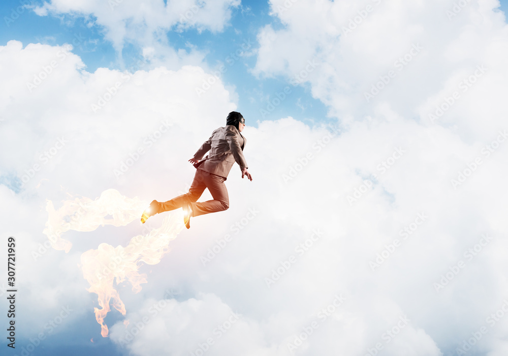 Businessman in suit and aviator hat flying in sky