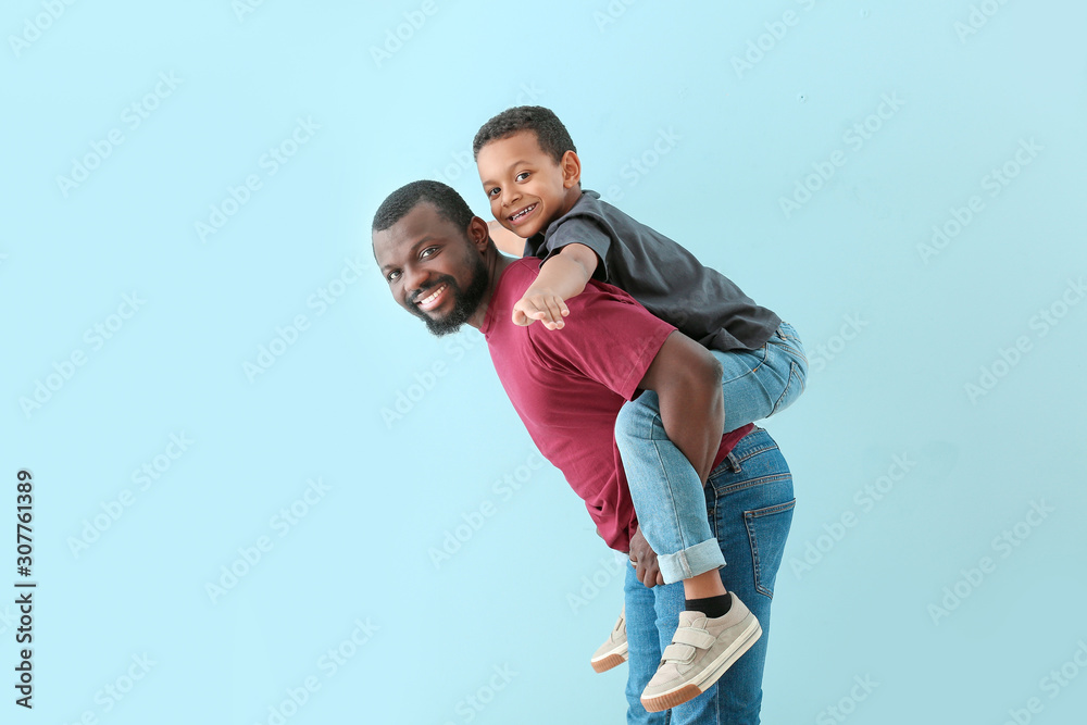 Portrait of African-American man with his little son on color background