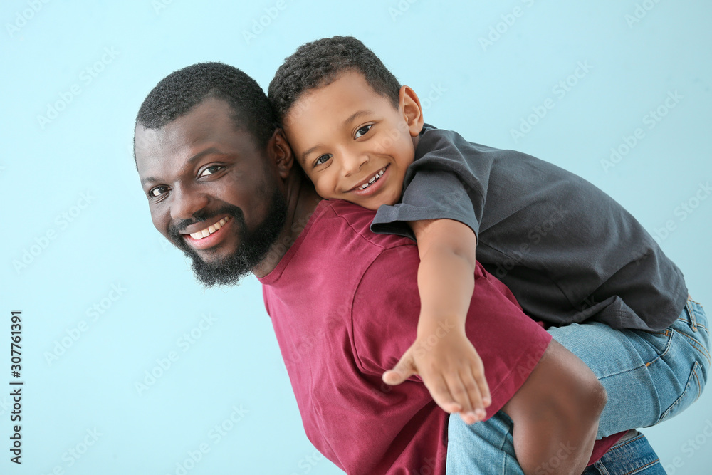 Portrait of African-American man with his little son on color background