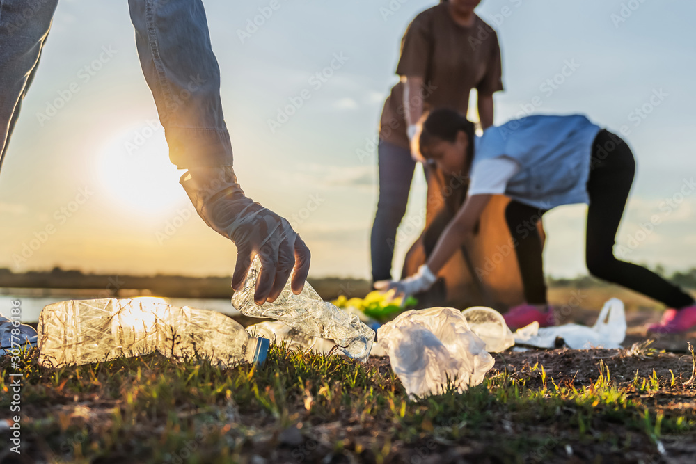 people volunteer keeping garbage plastic bottle into black bag at park near river in sunset