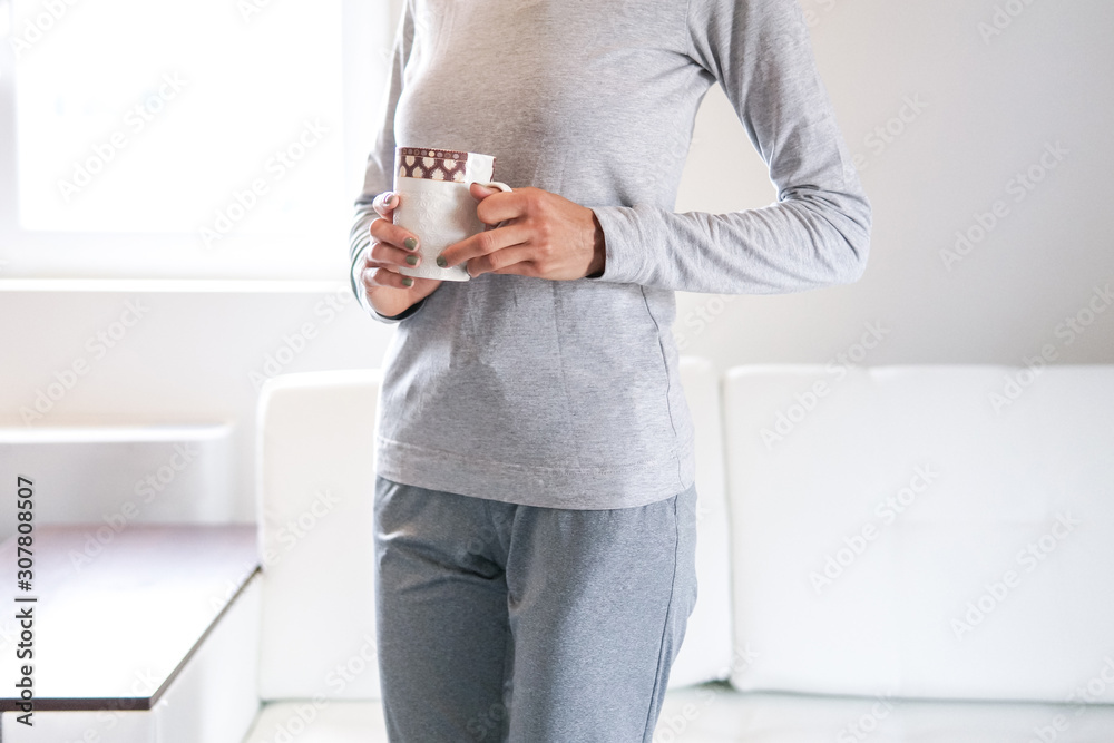 Young woman drinking coffee or tea with morning light in white kitchen