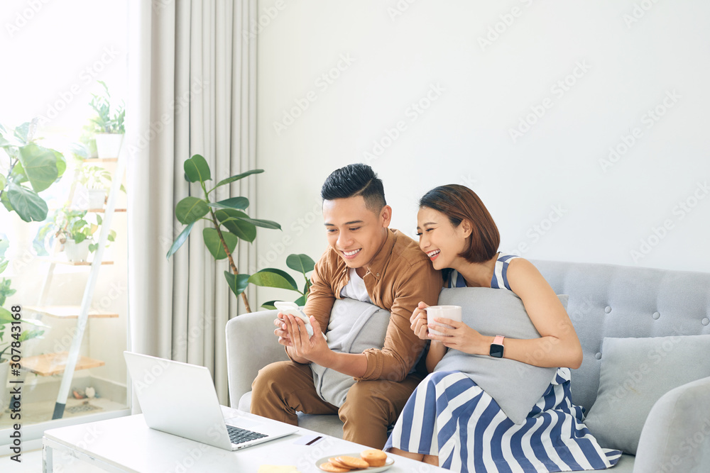 Beautiful couple enjoying together when watching smartphone, laptop at home.