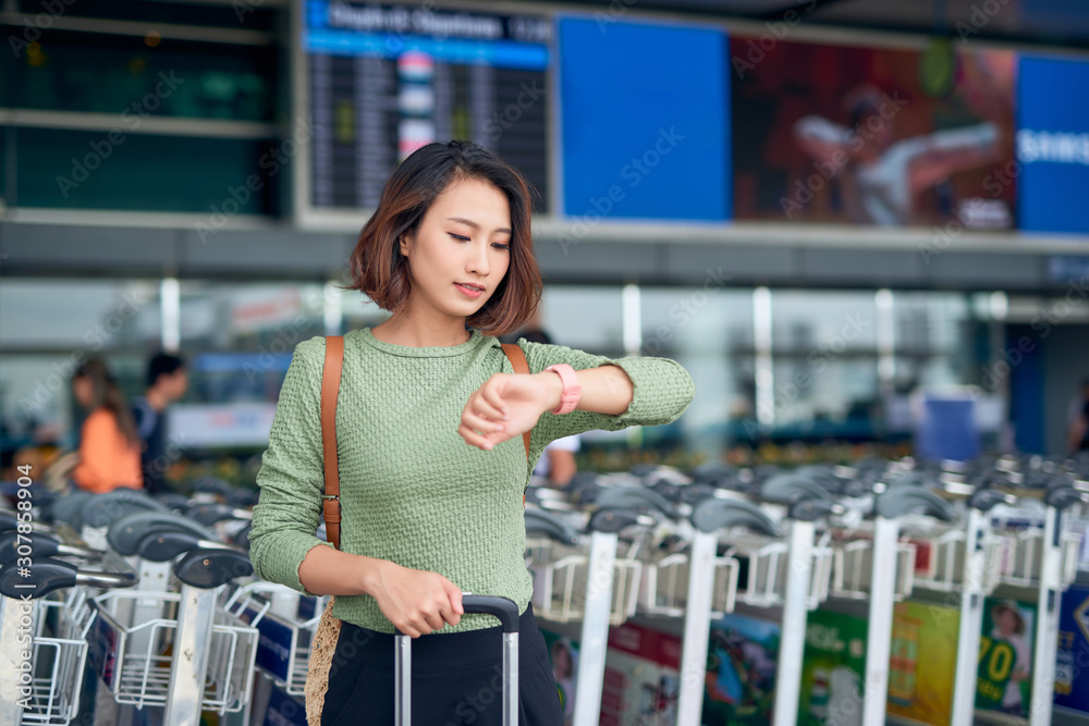 漂亮的年轻女子提着行李箱站在机场等公交车。