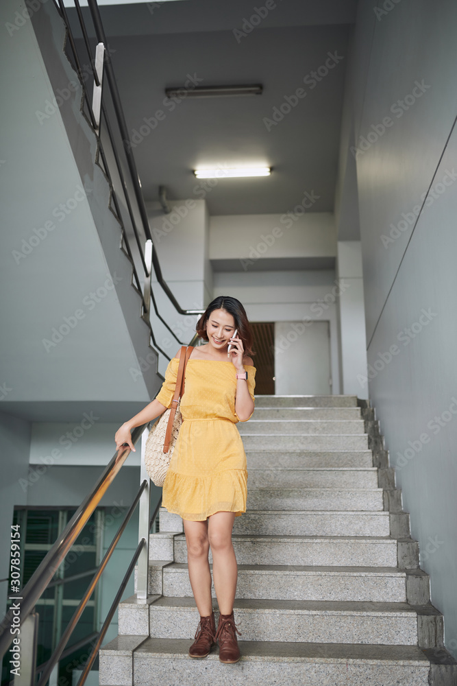 Happy young woman walking downstairs, talking on mobile phone