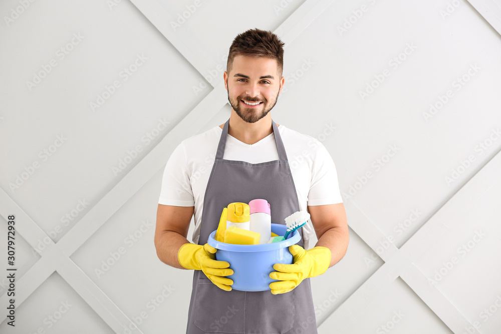 Male janitor with cleaning supplies on grey background