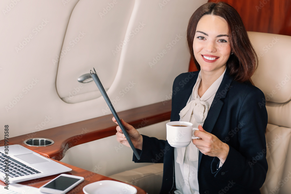 Businesswoman drinking coffee on board the modern private airplane