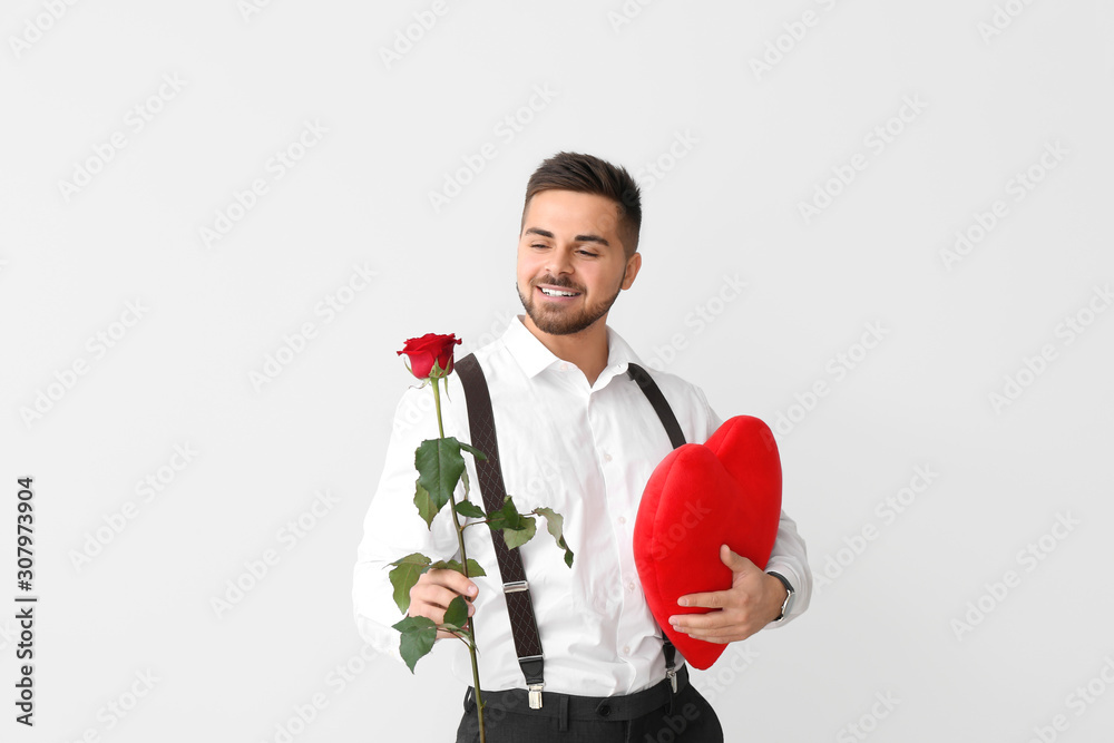 Handsome man with flower and red heart on light background. Valentines Day celebration