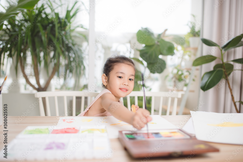 可爱的亚洲小女孩在家里用纸、水彩和画笔画画。