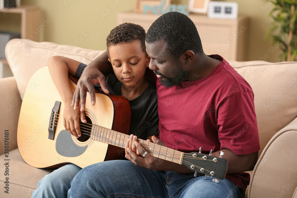 African-American man teaching his little son to play guitar at home