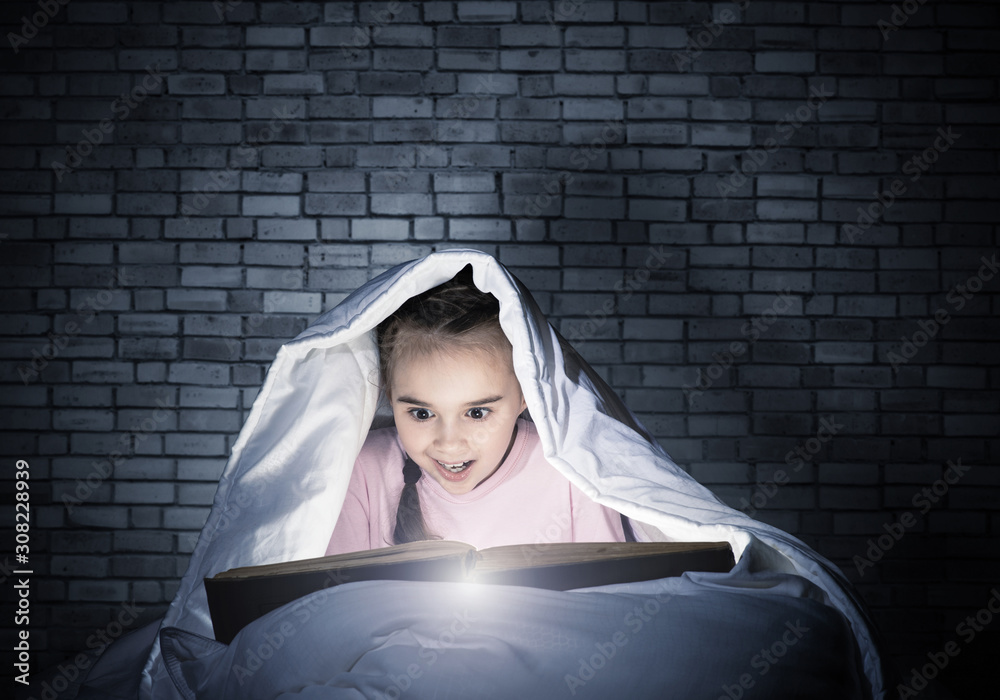 Happy little girl reading book in bed