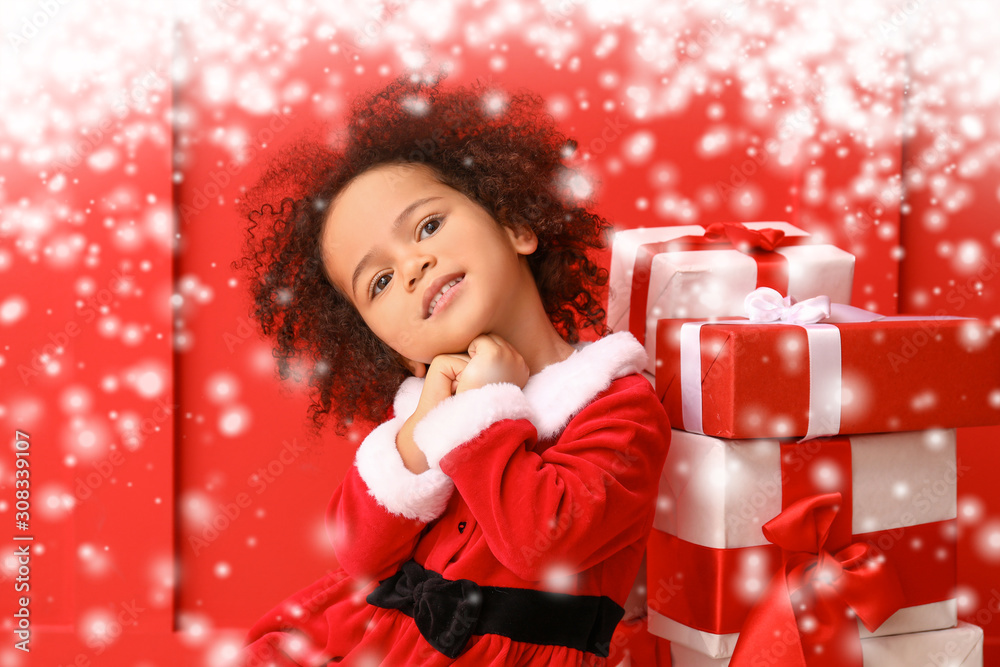 Little African-American girl in Santa costume and with gifts on color background with snow