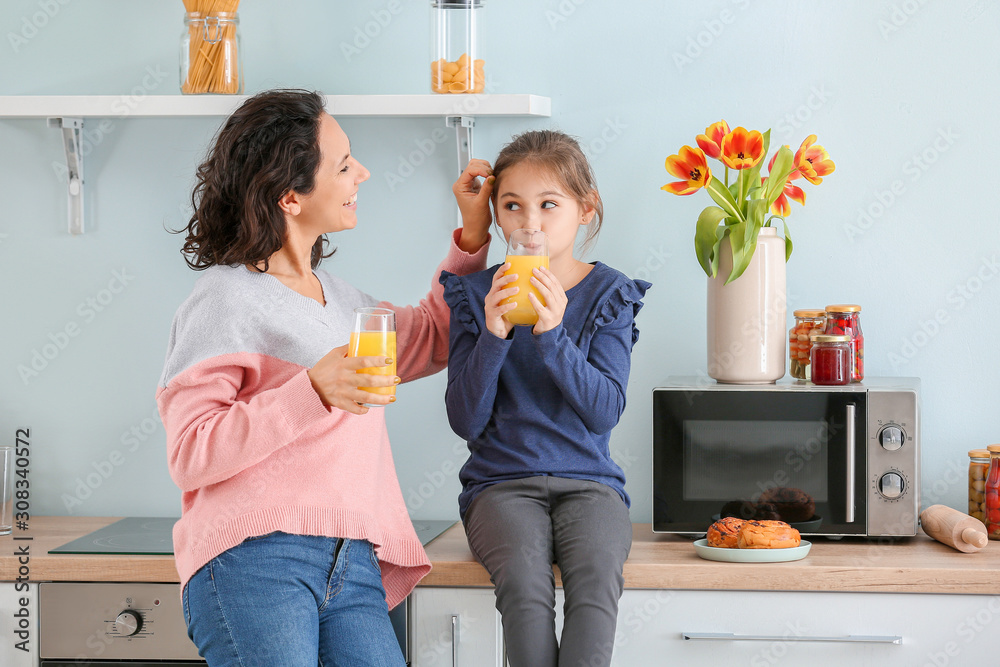 Little girl with her mother drinking juice in kitchen