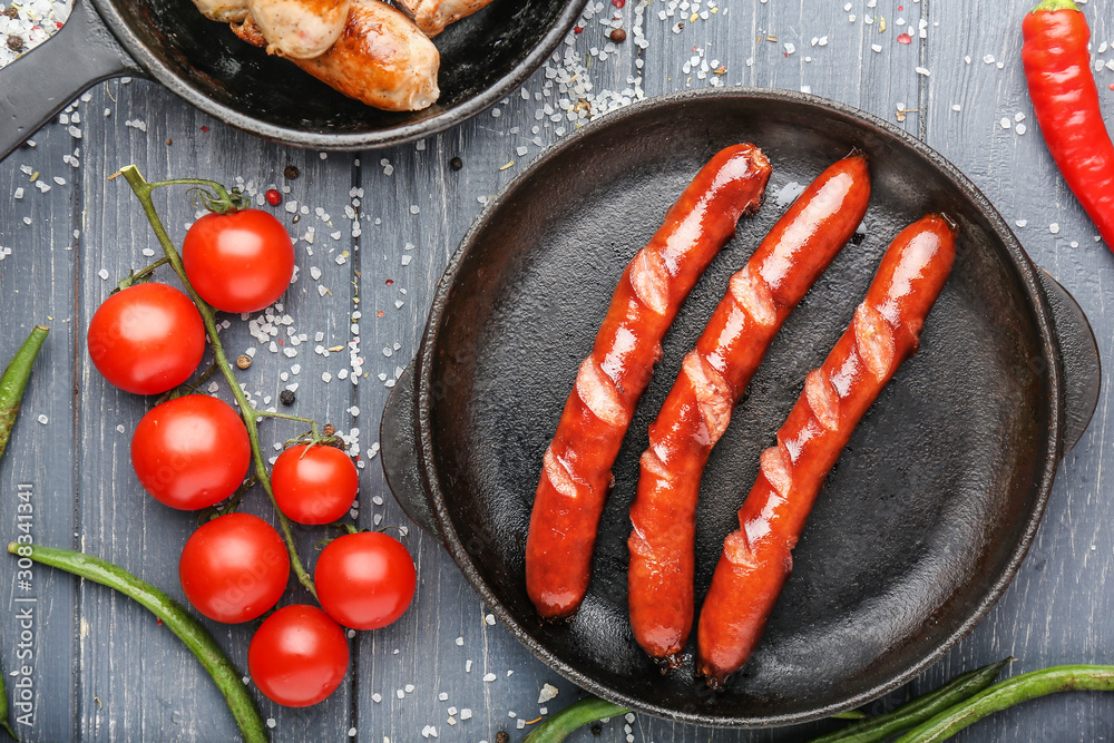 Frying pan with tasty grilled sausages on wooden background