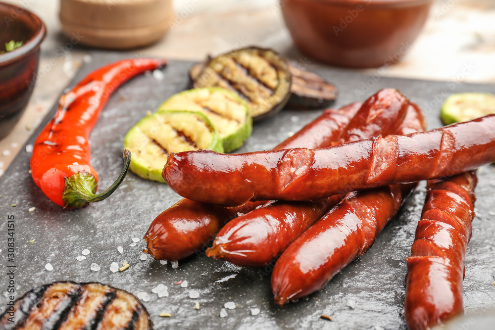 Tasty grilled sausages with vegetables on slate plate