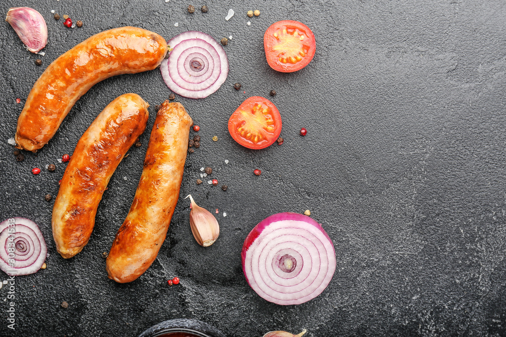 Tasty grilled sausages with vegetables and spices on dark background