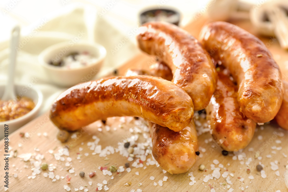 Tasty grilled sausages with spices on wooden board, closeup