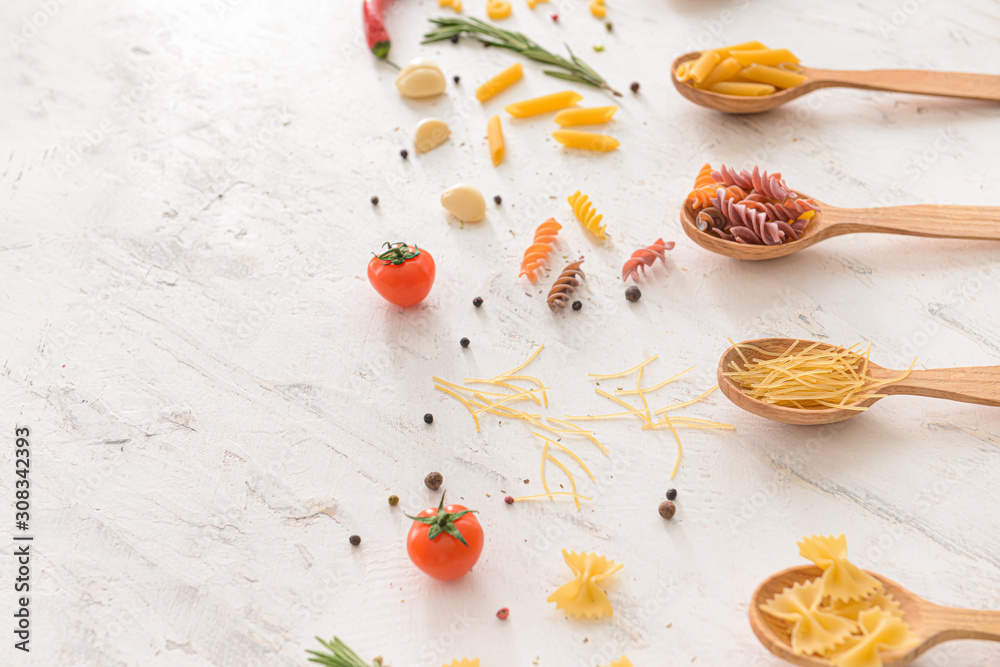 Spoons with different uncooked pasta on white background