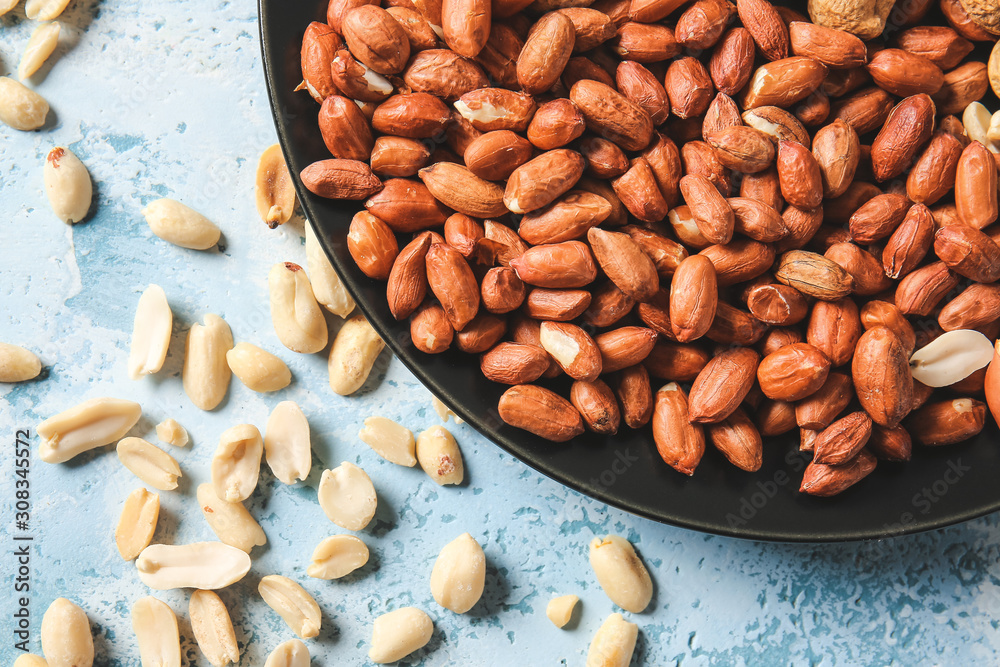 Plate with peanuts on color background