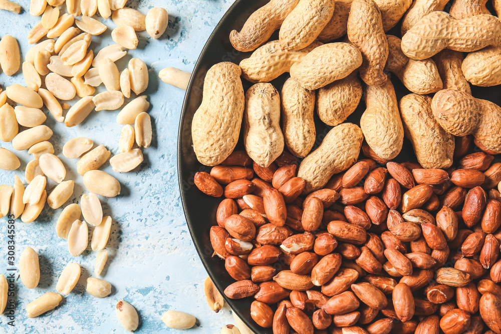 Plate with peanuts on color background