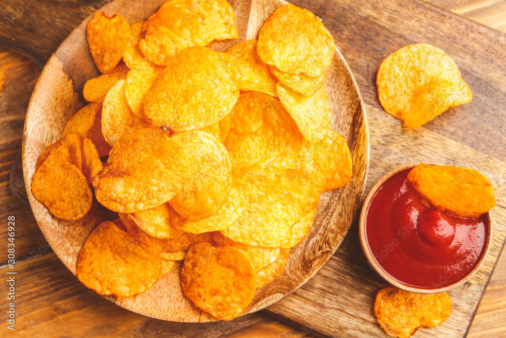 Tasty potato chips and tomato sauce on table