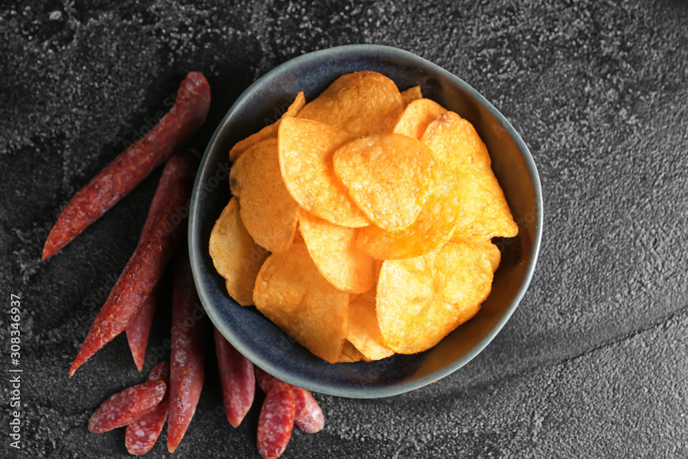 Bowl with tasty potato chips and sausages on table