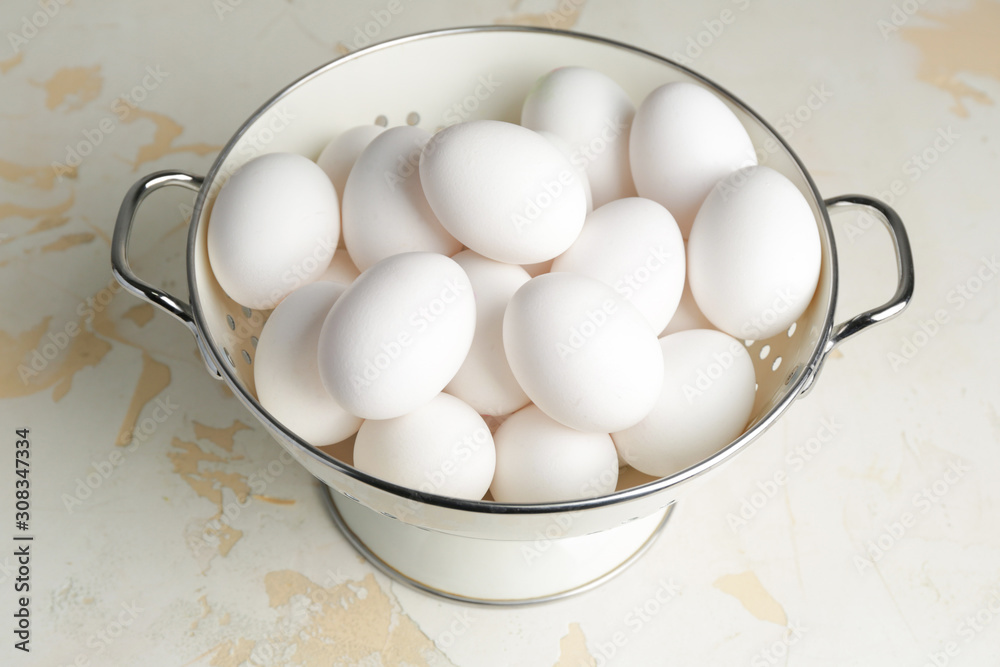 Colander with fresh raw eggs on table