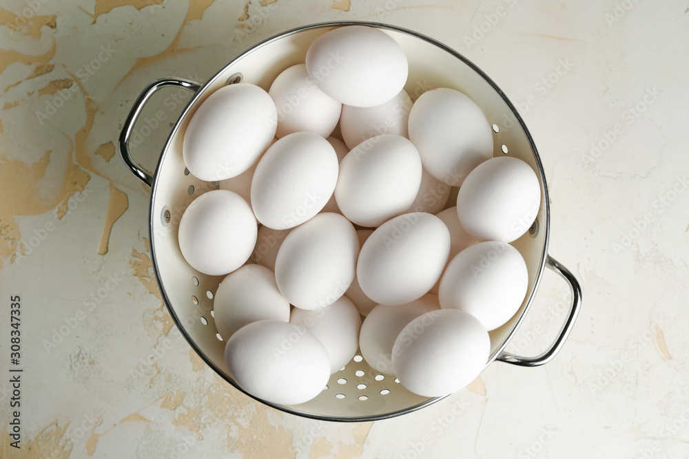 Colander with fresh raw eggs on table