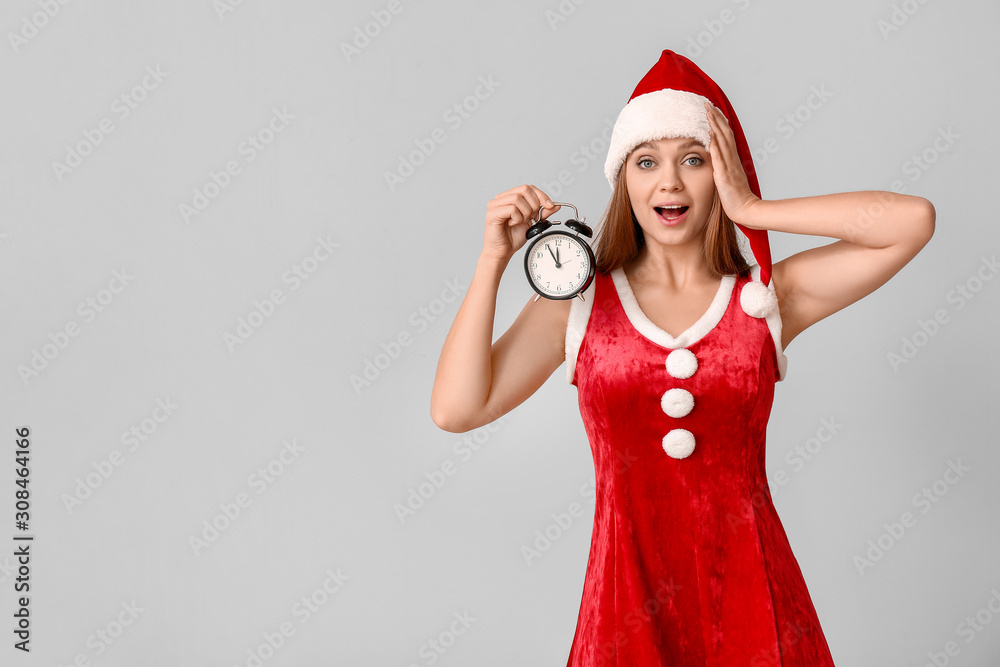 Surprised young woman in Santa costume and with alarm clock on light background. Christmas countdown