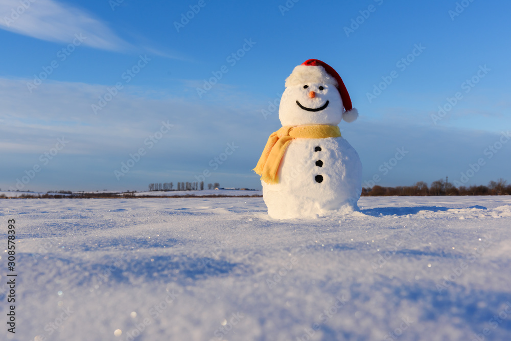 雪地上戴着红色圣诞老人帽和黄色鳞片的有趣雪人。圣诞节和新年背景