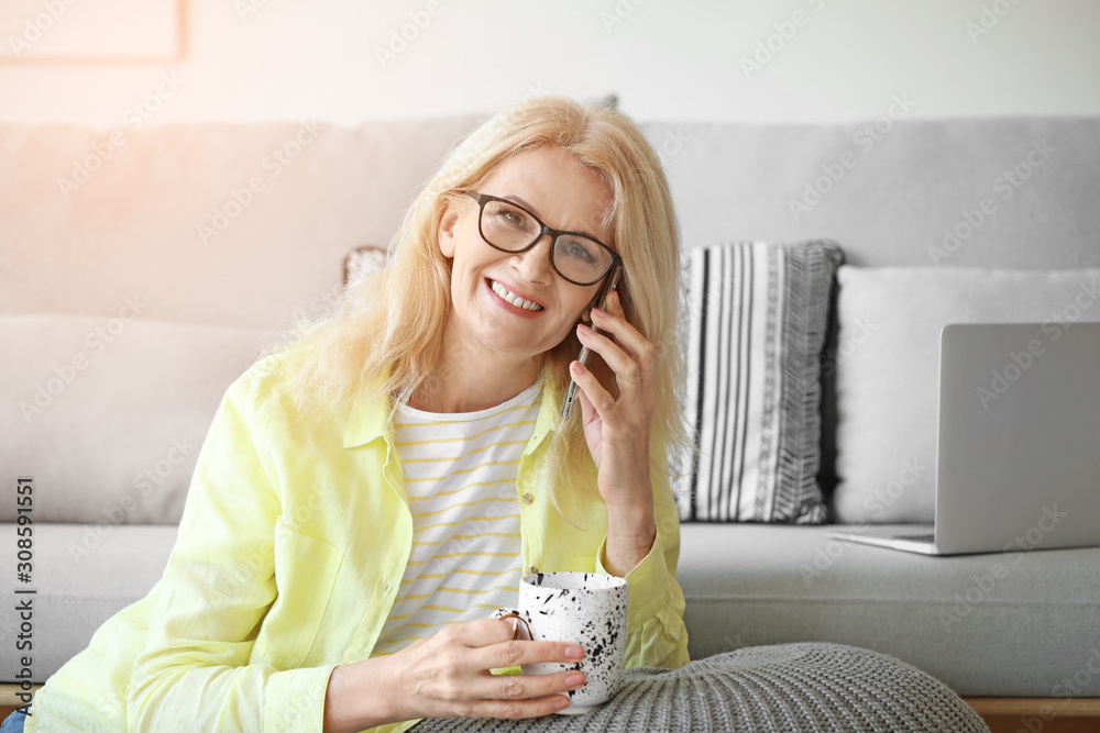 Portrait of beautiful mature woman talking by phone and drinking coffee at home