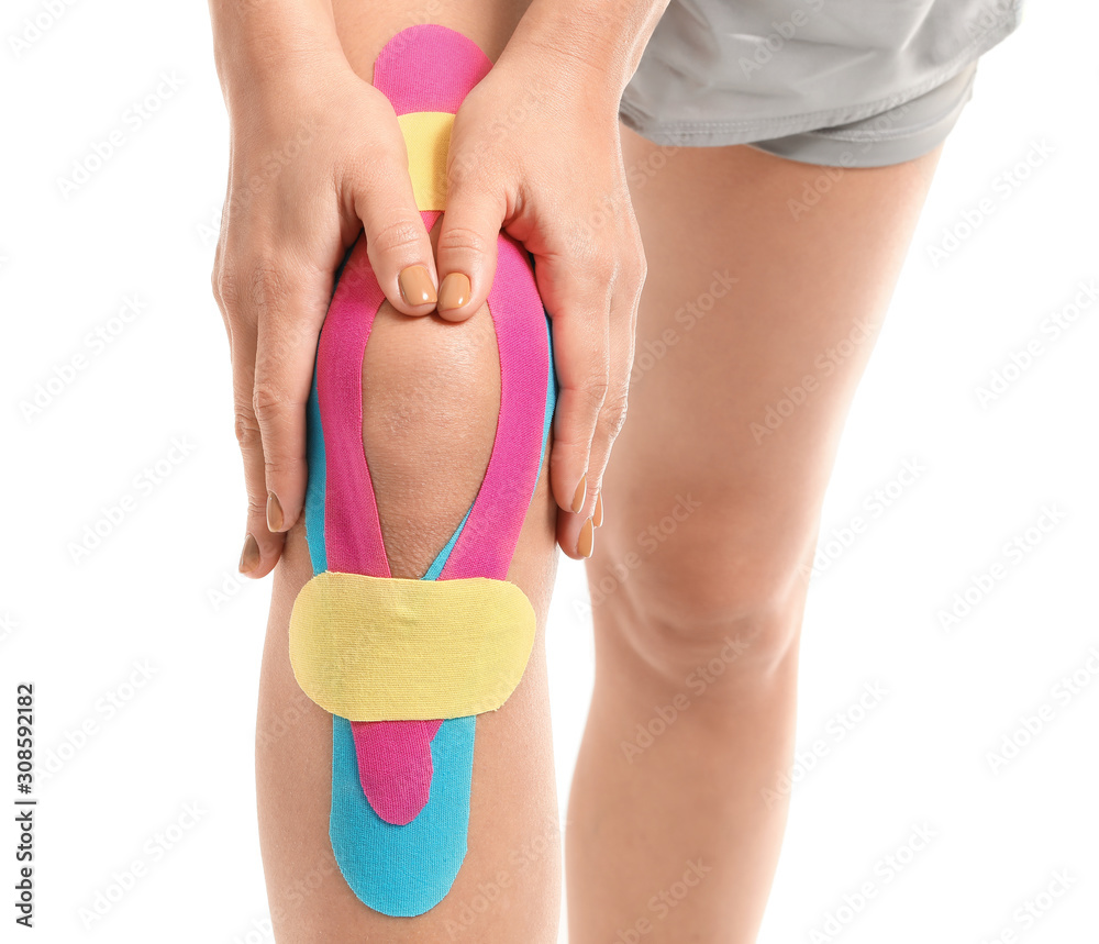 Sporty woman with physio tape applied on knee against white background, closeup