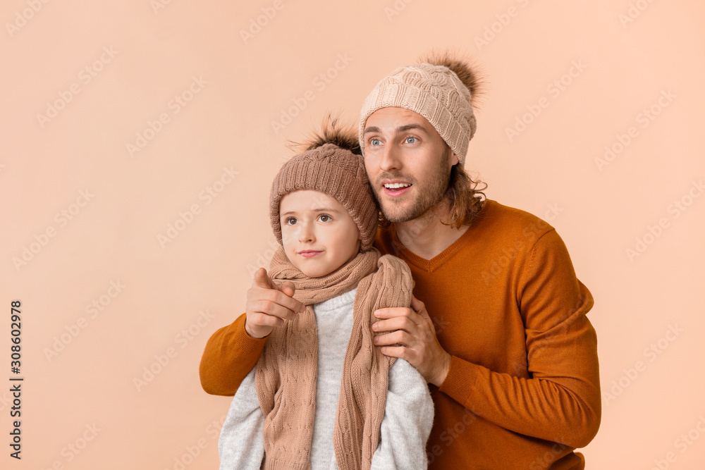 Man and his son in winter clothes on color background