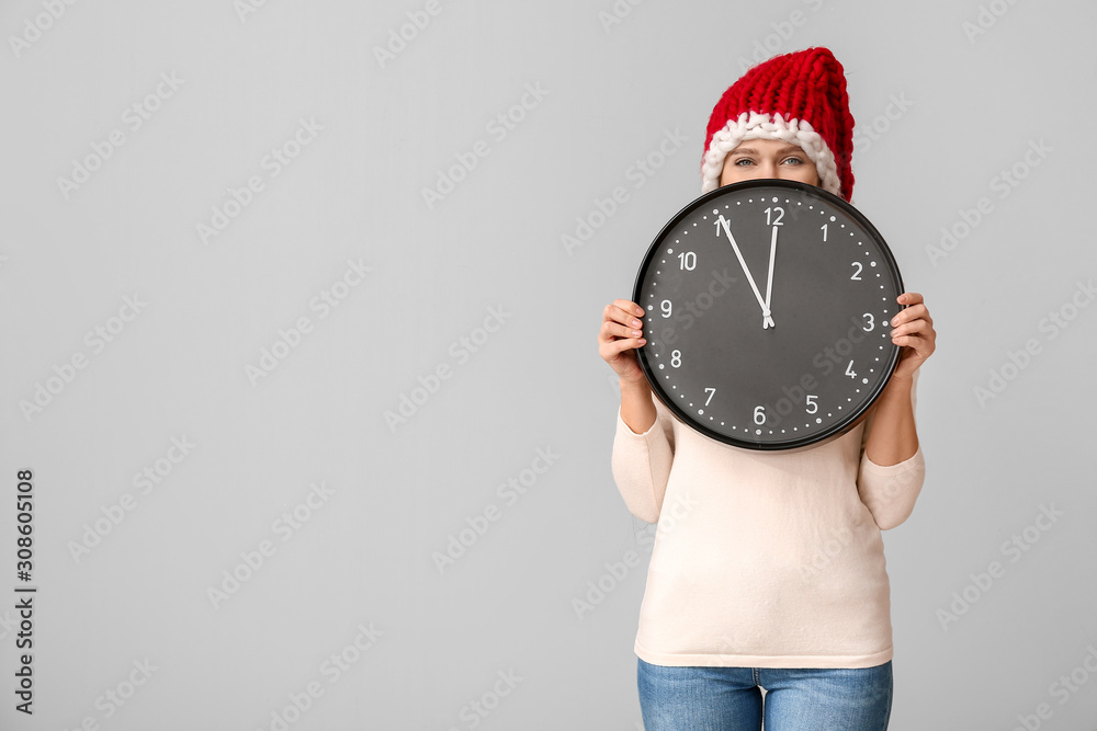 Young woman in Santa hat and with clock on light background. Christmas countdown concept