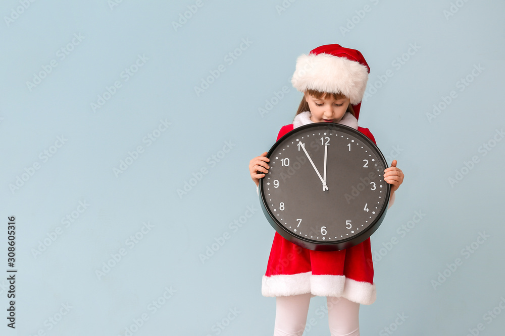 Little girl in Santa costume and with clock on color background. Christmas countdown concept