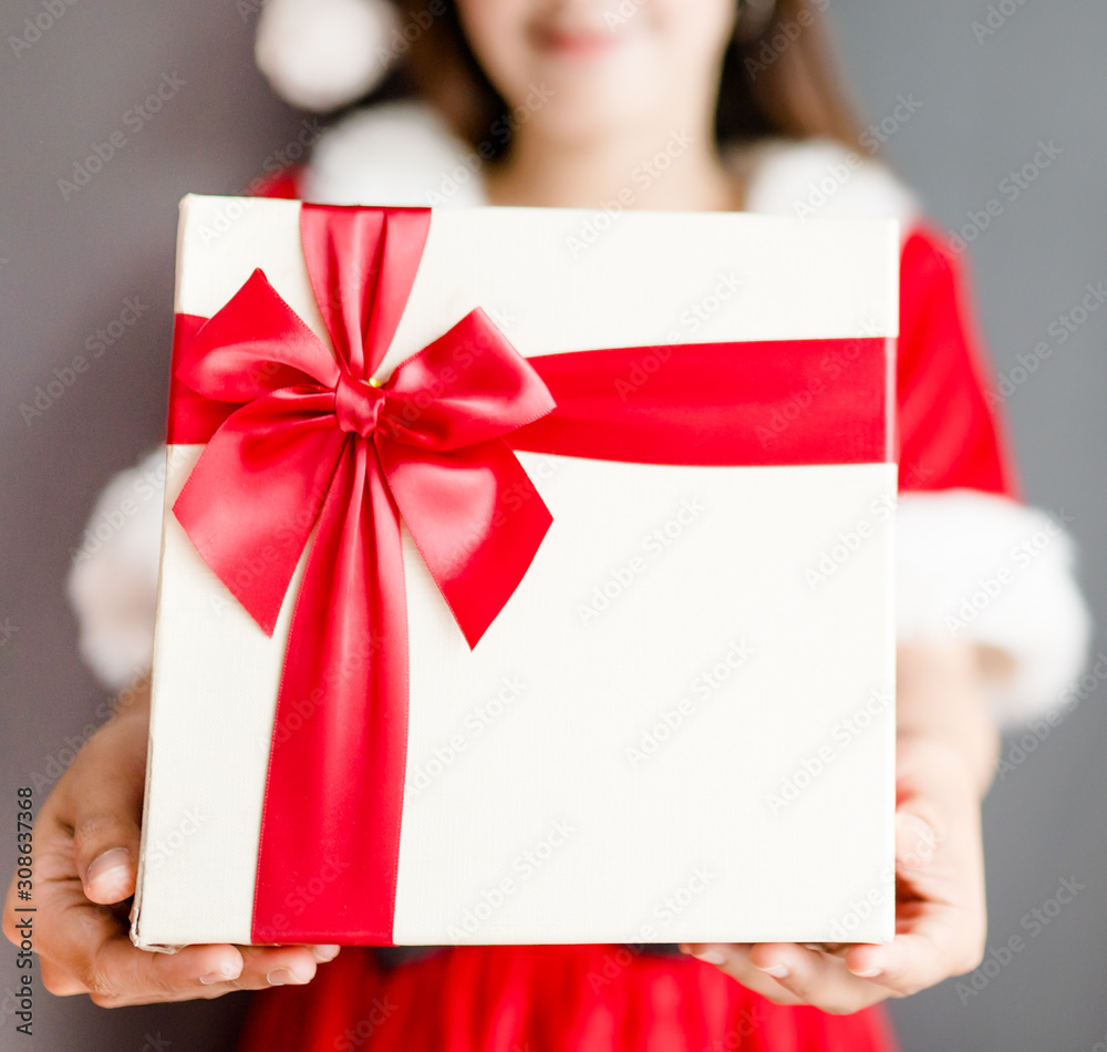 Portrait of young asian caucasian woman girl wearing santa costume and holding gift box on gray back