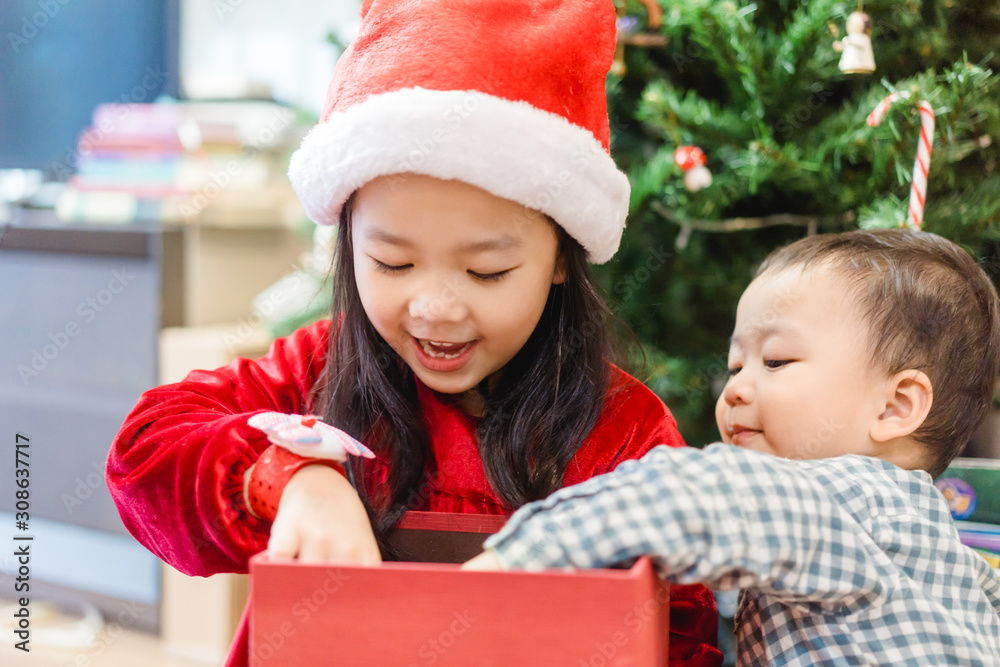 Sibling boy and girl smile and excited and open red gift box on christmas tree background.Childhood 