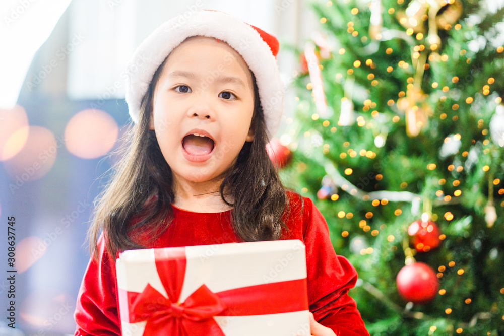 Little asian girl smile and excited and holding red gift box on christmas tree and white background.