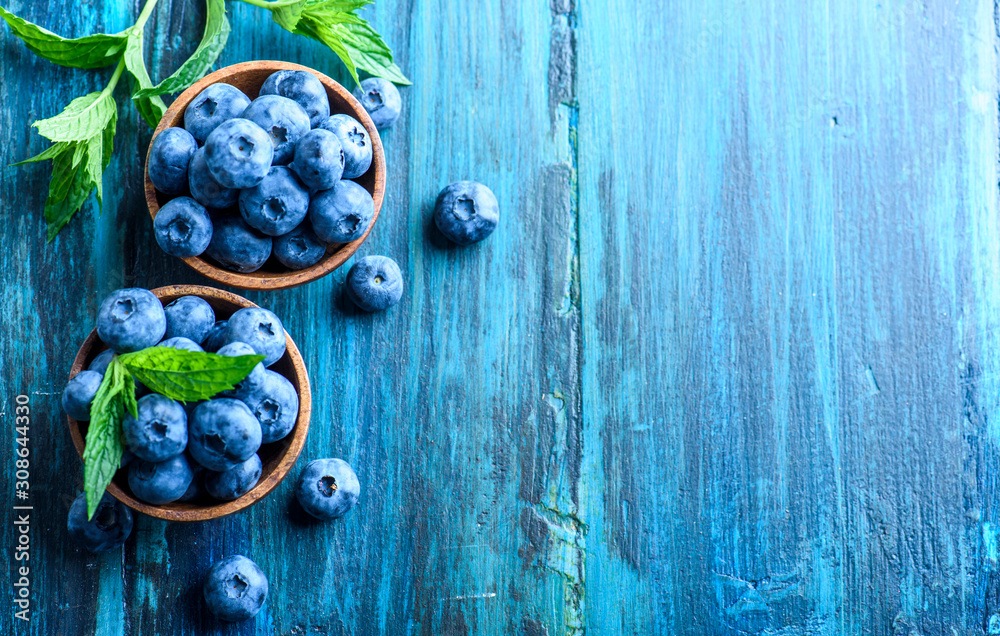 Bowl of fresh blueberries on blue rustic wooden table from above.