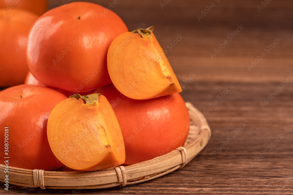 Sliced sweet persimmon kaki in a bamboo sieve basket on dark wooden table with red brick wall backgr