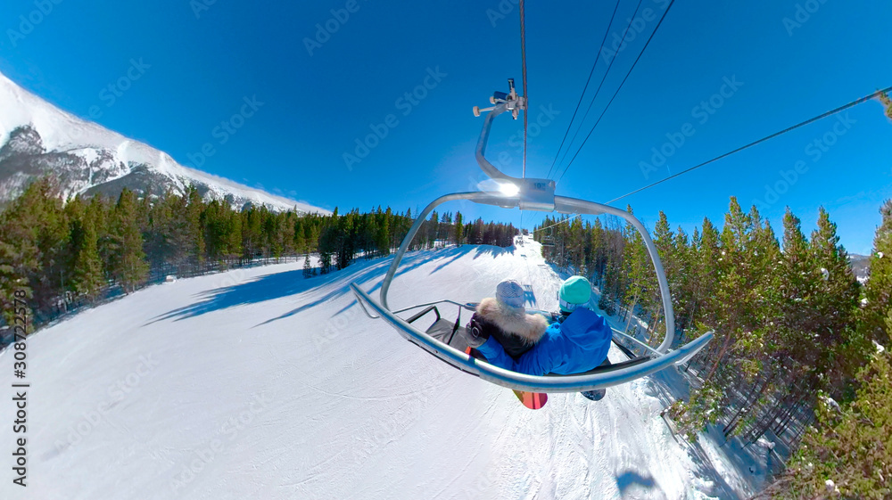 SELFIE: Snowboarding couple rides the chairlift and observe the snowy mountains