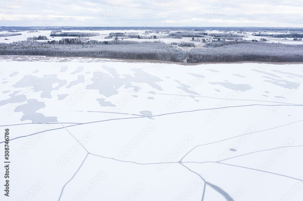 Aerial drone view of a partially frozen lake with unfrozen patches and ice cracks on a winter mornin