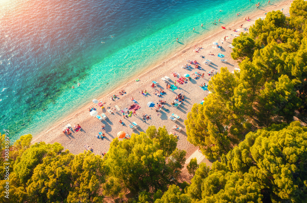 Aerial view of sandy beach with colorful umbrellas, lying people, clear sea bay with transparent blu