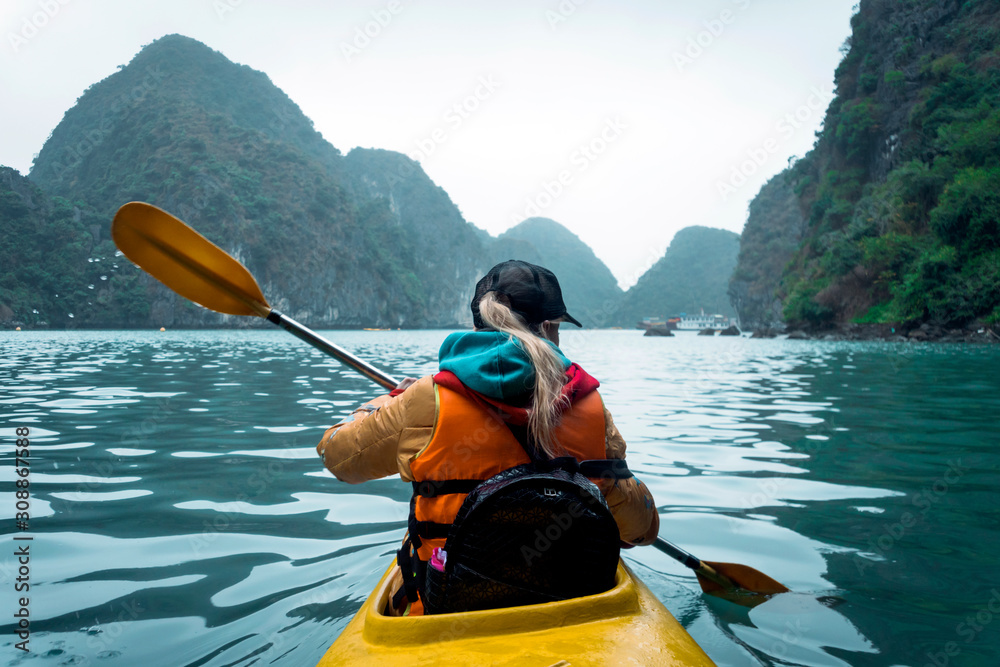 年轻漂亮的女人漂浮在皮划艇上，漂浮在露出大海的岩石之间。女孩在划船